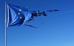 The EU flag torn and with knots in the wind on blue sky