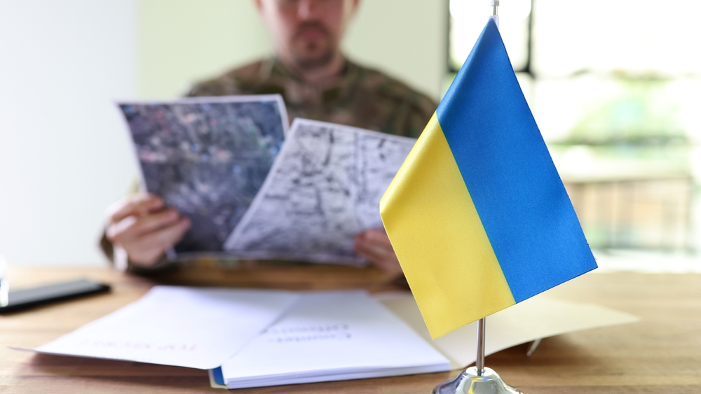 Ukraine flag in front of military man holding in hands secret plans of Ukrainian counteroffensive operation